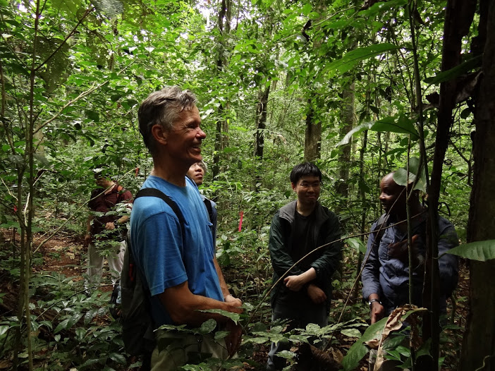 Joe Wright smiling in a blue shirt in the forest on Barro Colorado Island, surrounded by a few other scientists 
