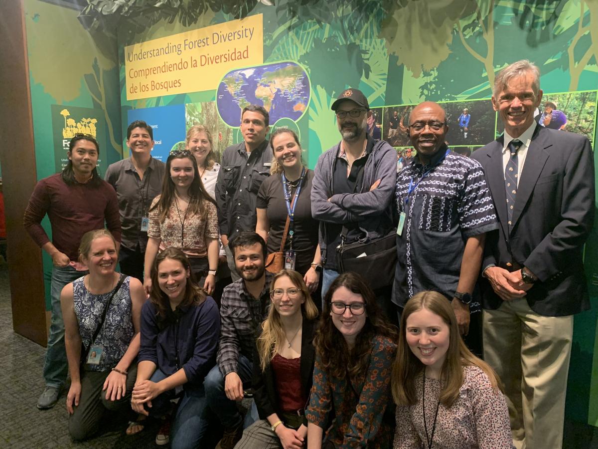 A group of ForestGEO employees standing in front of a colorful display at the BCI exhibit in the National Museum of Natural History