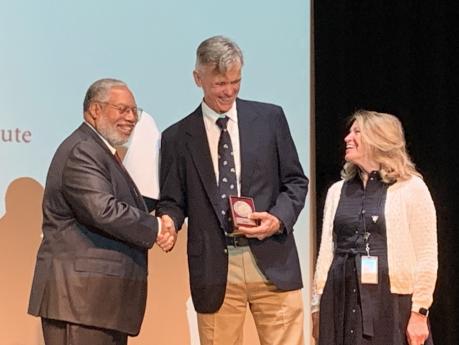 Dr. Wright being present his award on stage, shaking hands with Lonnie Bunch and smiling with Ellen Stofan 
